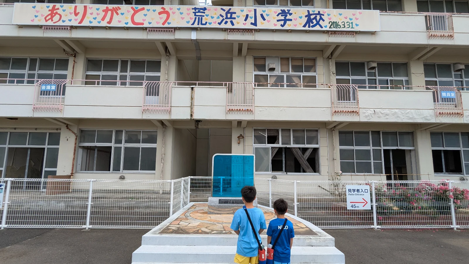 Children stand before the memorial monument outside Arahama Elementary School in Sendai, a preserved site honoring the Great East Japan Earthquake.