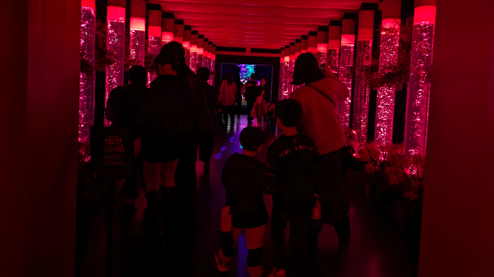 Children walking through the illuminated Goldfish Path tunnel with torii-gate style aquariums at Art Aquarium Museum Ginza.