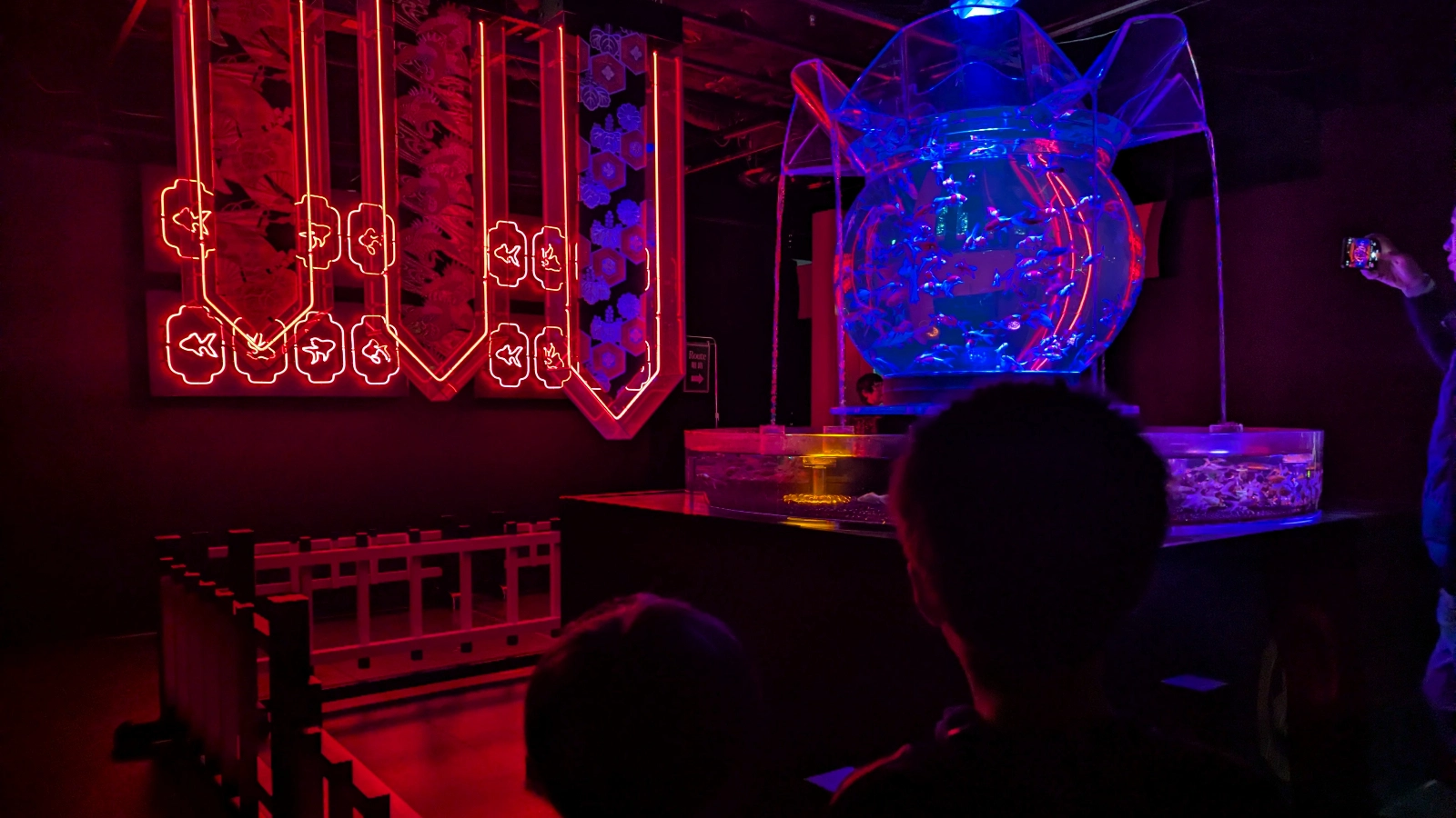 Kids watching a neon-lit goldfish tank with traditional Japanese patterns at Art Aquarium Museum Ginza in Tokyo.