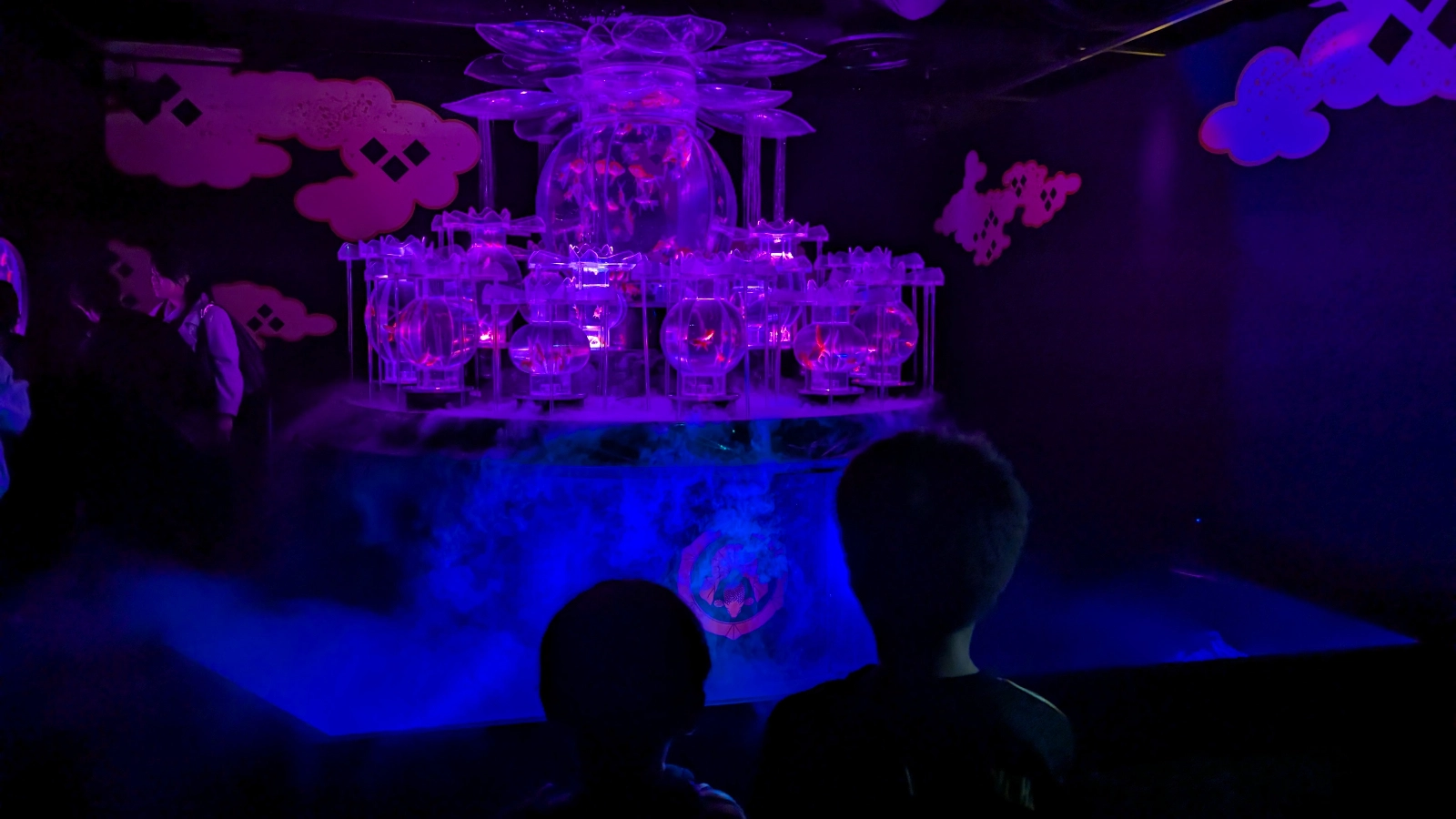 Children watching a glowing purple goldfish installation surrounded by mist at Art Aquarium Museum Ginza.