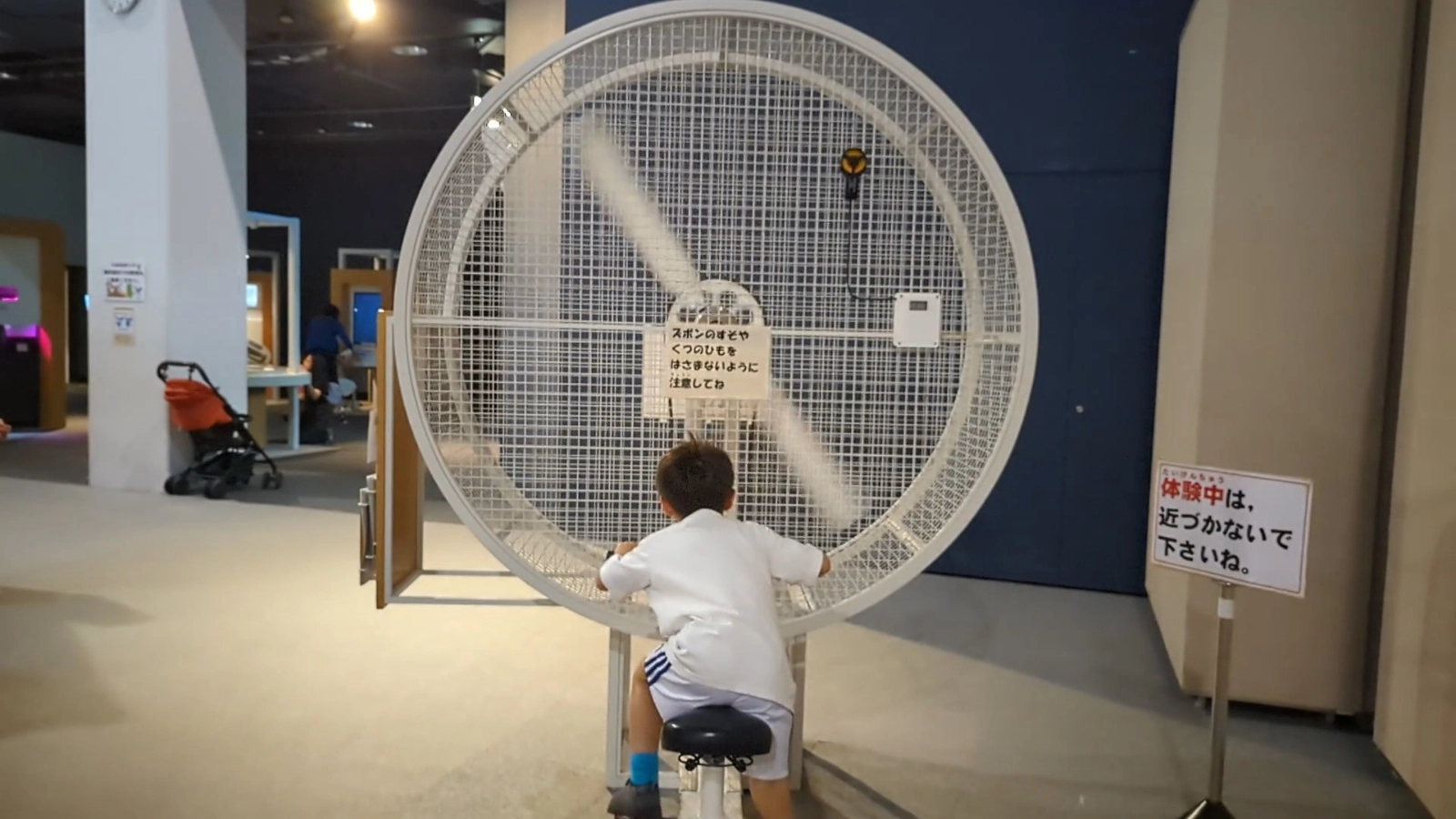 A child pedals a stationary bike to power a large fan at Asahikawa Science Museum, part of the energy and motion exhibits designed for kids.