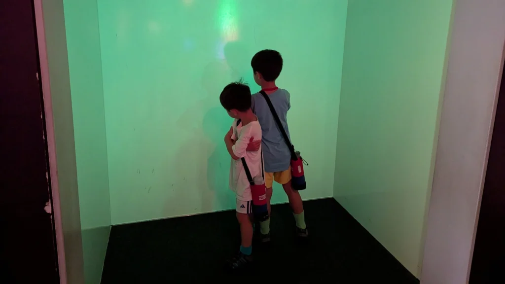Children pose playfully in the shadow and light room at Asahikawa Science Museum, exploring how light creates silhouettes on a colored wall.