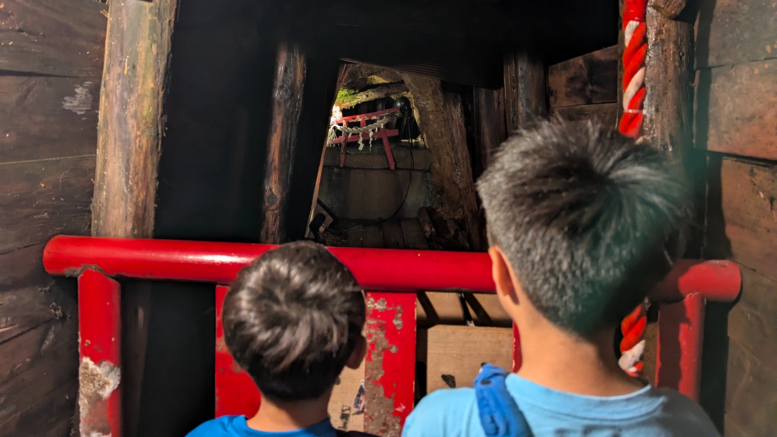 Two children look toward a small red torii gate hidden inside the tunnels of the Ashio Copper Mine Museum in Nikko, Japan.