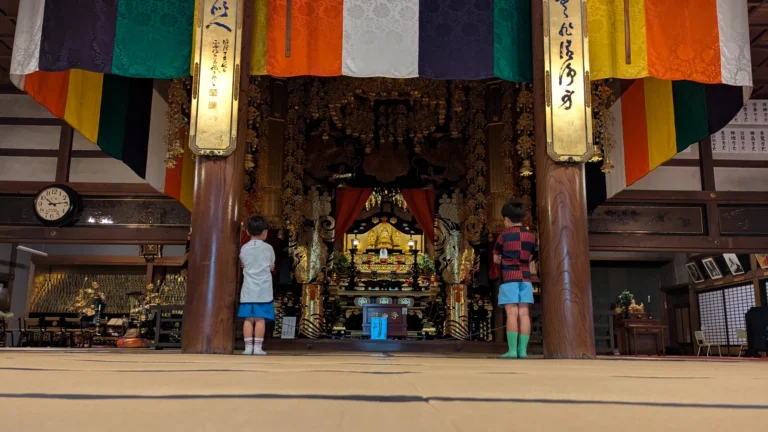 Two children standing quietly inside a traditional Japanese temple, observing the ornate altar during a family visit.