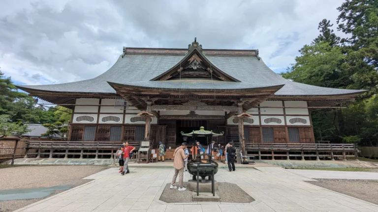 Visitors standing in front of the main worship hall at Chusonji Temple in Hiraizumi, a historic World Heritage Site surrounded by trees.