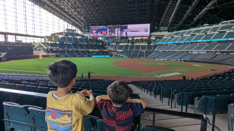 Two kids watch the baseball field at Es Con Field Hokkaido stadium, enjoying the family-friendly atmosphere before a game.