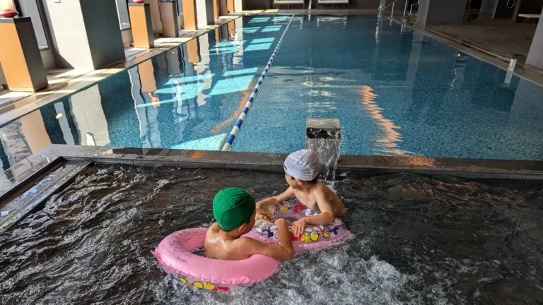 Luca & Nico wearing swim caps and goggles play in an indoor pool at a family hotel in Japan.