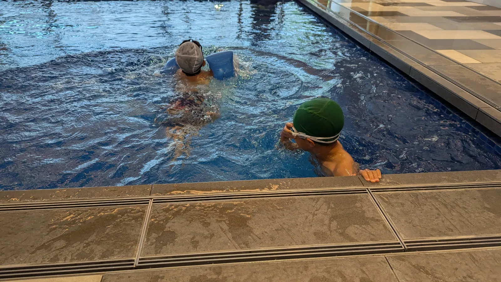 Luca & Nico wearing swim caps and goggles play in an indoor pool at a family hotel in Japan.