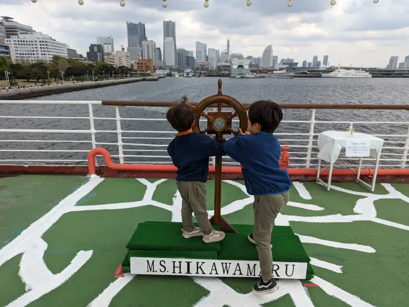 Luca & Nico exploring the historic Hikawa Maru ship in Yokohama, with the modern city skyline in the background, a perfect blend of history and adventure for family travel in Japan.