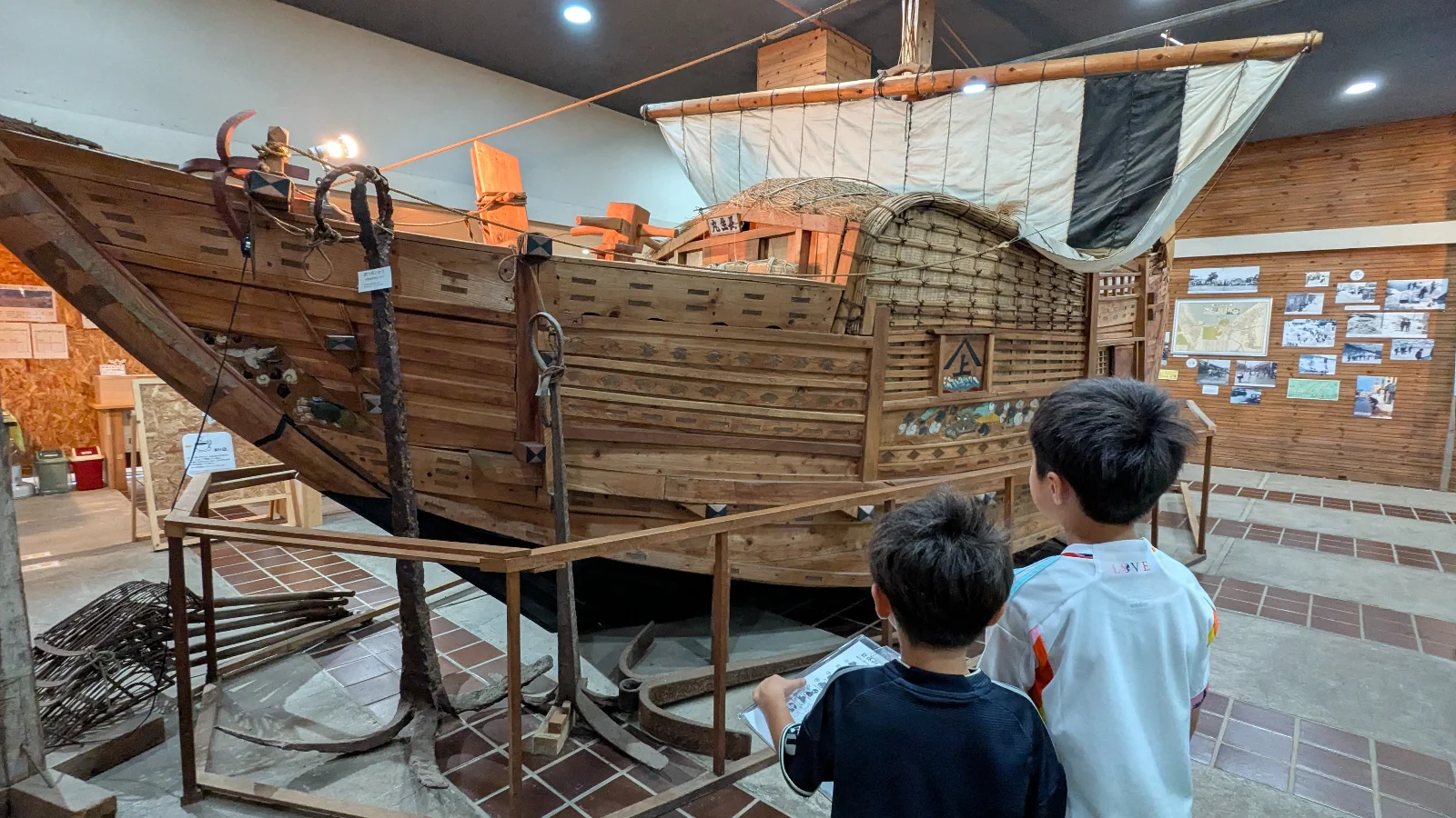 Two kids observe a large wooden fishing boat display at the Yoichi Fisheries Museum near Otaru, learning about Hokkaido’s maritime history.
