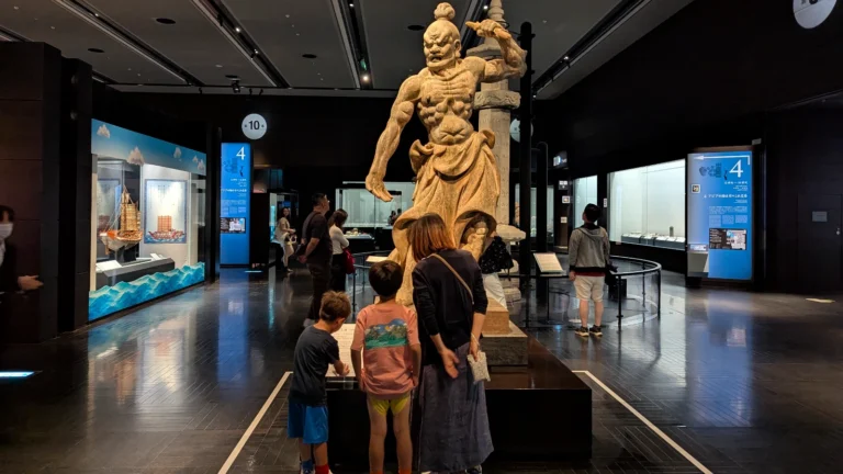 Luca & Nico exploring a dramatic guardian statue and historical ship exhibits inside the Kyushu National Museum in Fukuoka, one of the best indoor cultural attractions for kids in Japan.