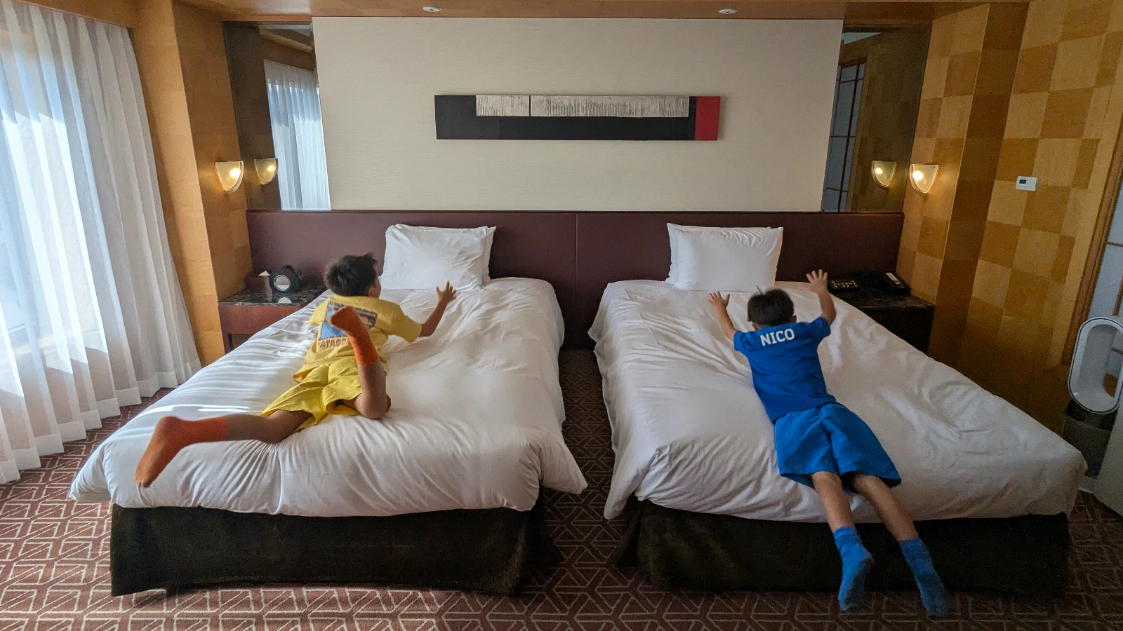 Luca & Nico jumping onto twin beds in a family room at Grand Hyatt Fukuoka hotel in Japan, showcasing kid-friendly accommodations.