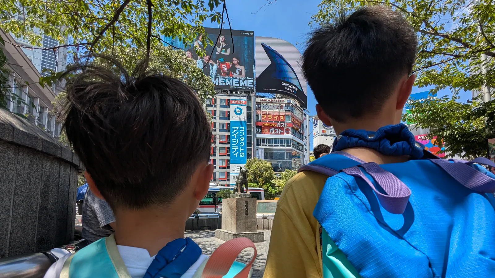 Luca & Nico with backpacks looking at the Hachiko Dog Statue (忠犬ハチ公像) in Shibuya, Tokyo, a famous landmark inspired by Hachi: A Dog’s Tale movie.