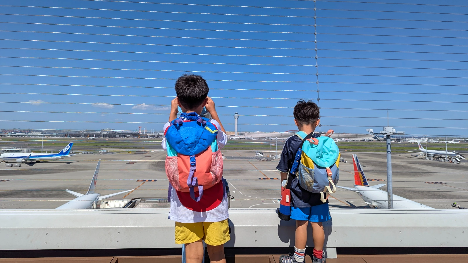 Luca & Nico with backpacks watching airplanes from the Haneda Airport observation deck in Tokyo, a perfect family-friendly travel moment