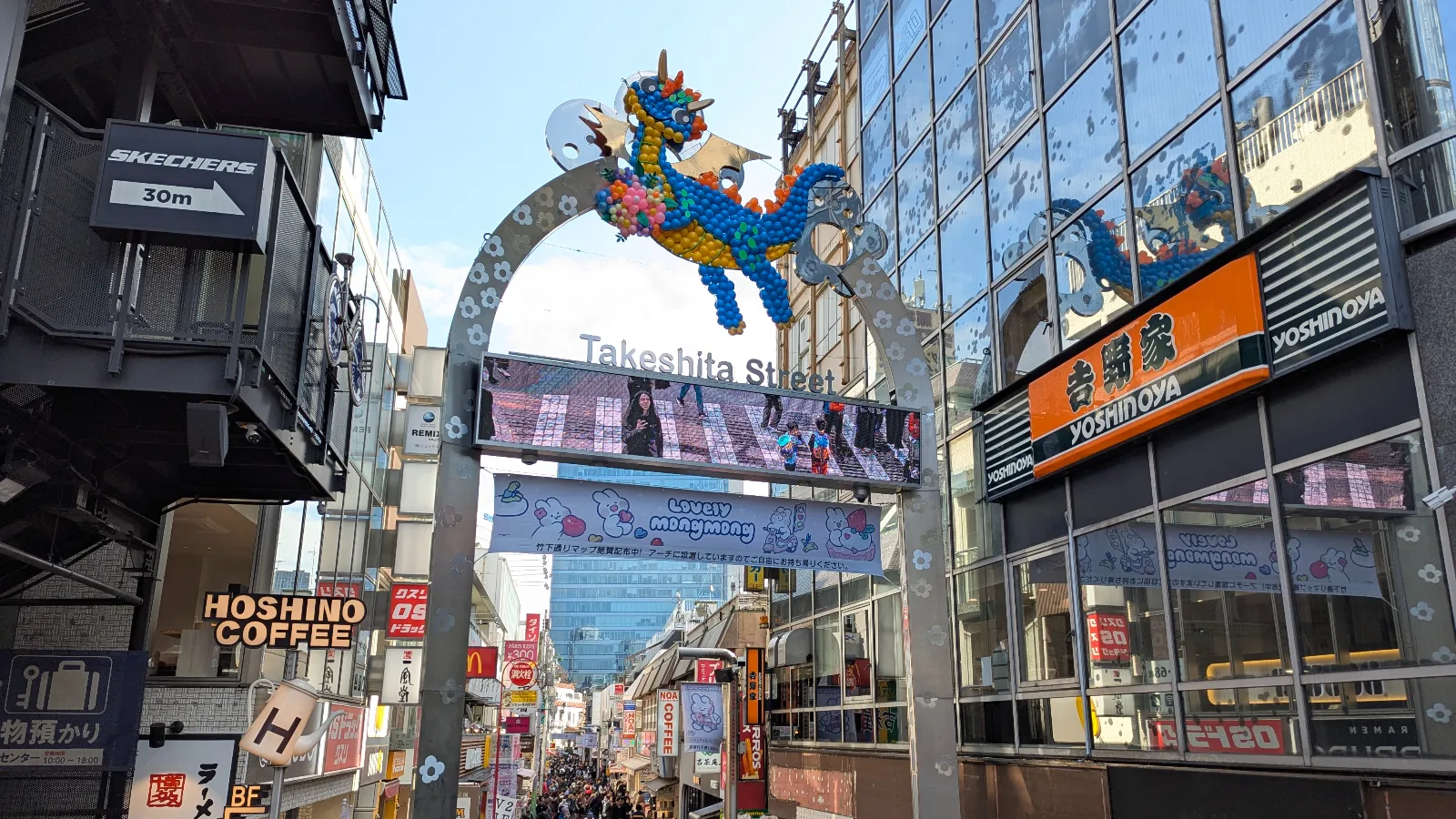 The colorful Takeshita Street entrance gate in Harajuku, Tokyo, featuring balloon art above the sign and a busy shopping street below.