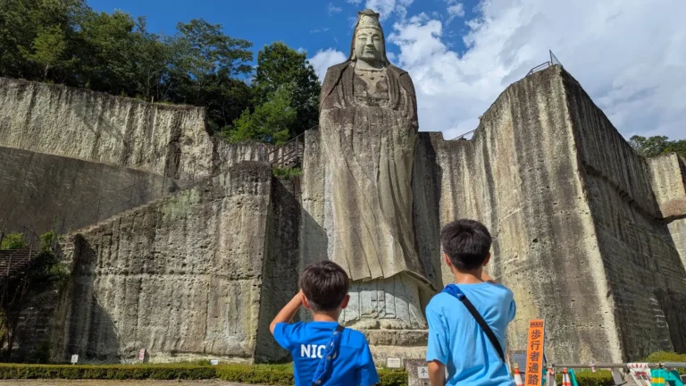 Two children look up at the towering Heiwa Kannon statue carved into the Oya stone cliffs in Utsunomiya, Japan.