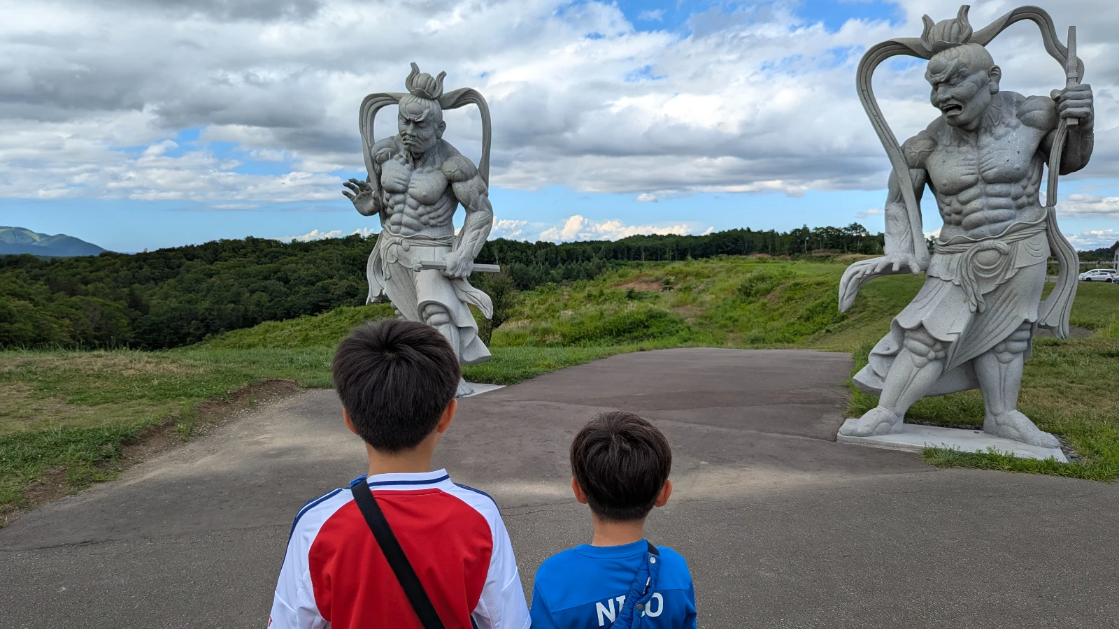 Children standing before the giant Nio guardian statues that mark the approach to the Hill of the Buddha in Sapporo, Hokkaido.