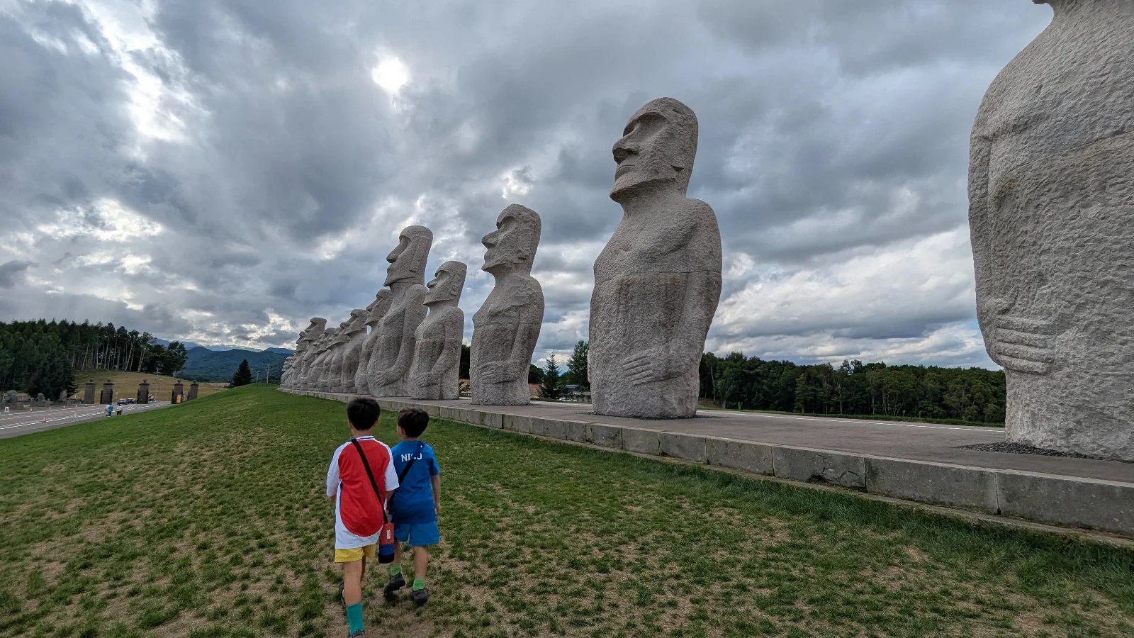 Kids walking beside the long row of Moai statues at Makomanai Takino Cemetery near the Hill of the Buddha in Sapporo, Hokkaido.