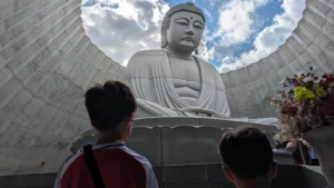 Two children looking up at the massive Buddha statue inside the Hill of the Buddha in Sapporo, Japan, designed by Tadao Ando.