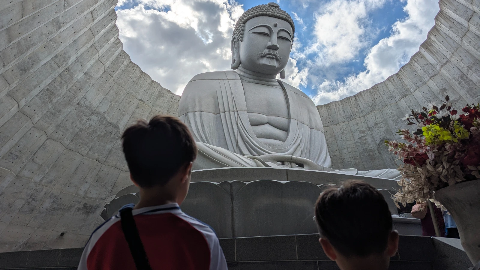 Two children looking up at the massive Buddha statue inside the Hill of the Buddha in Sapporo, Japan, designed by Tadao Ando.