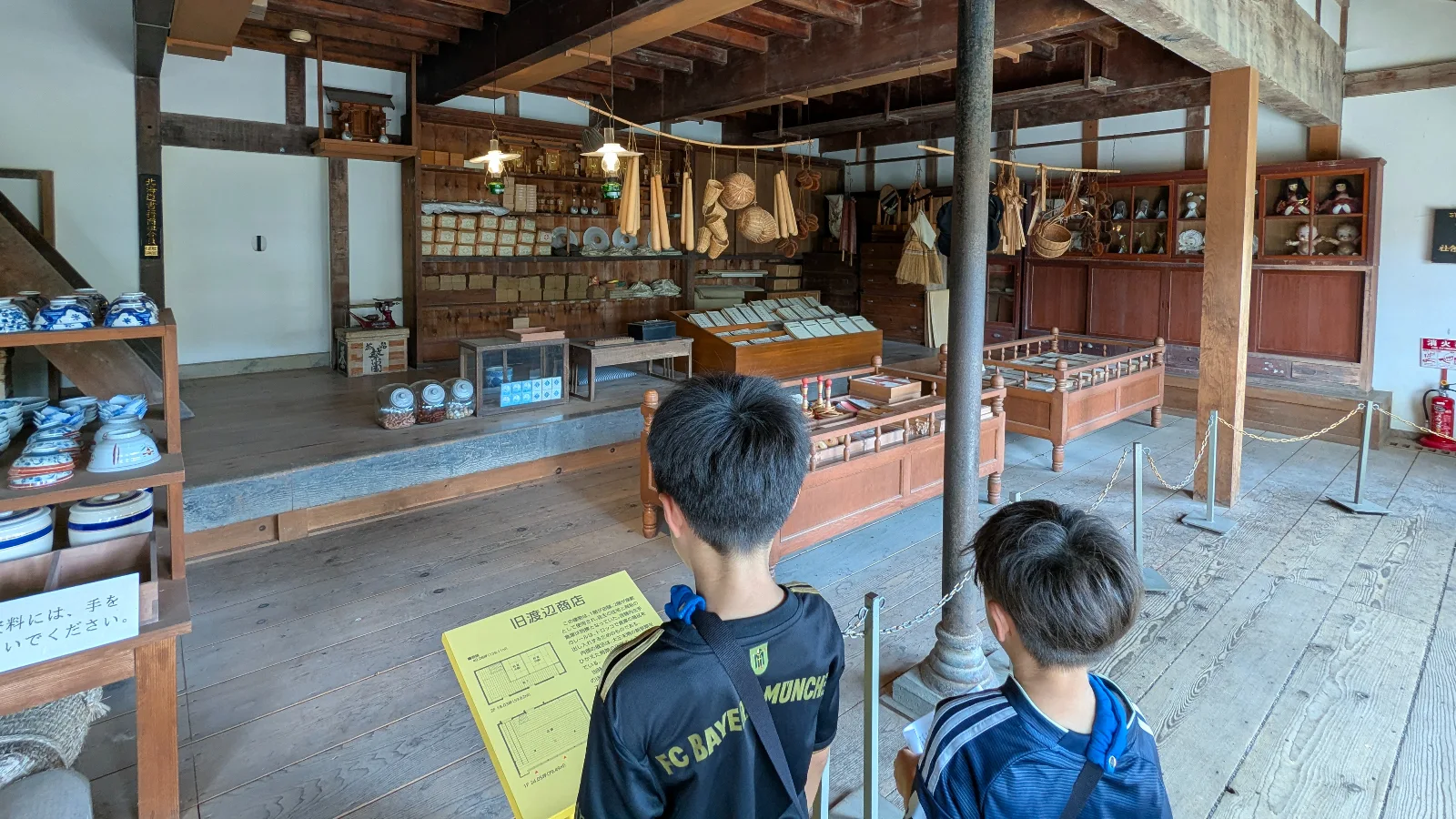 Two children explore a restored merchant shop filled with wooden shelves, traditional crafts, and vintage goods at the Historical Village of Hokkaido.