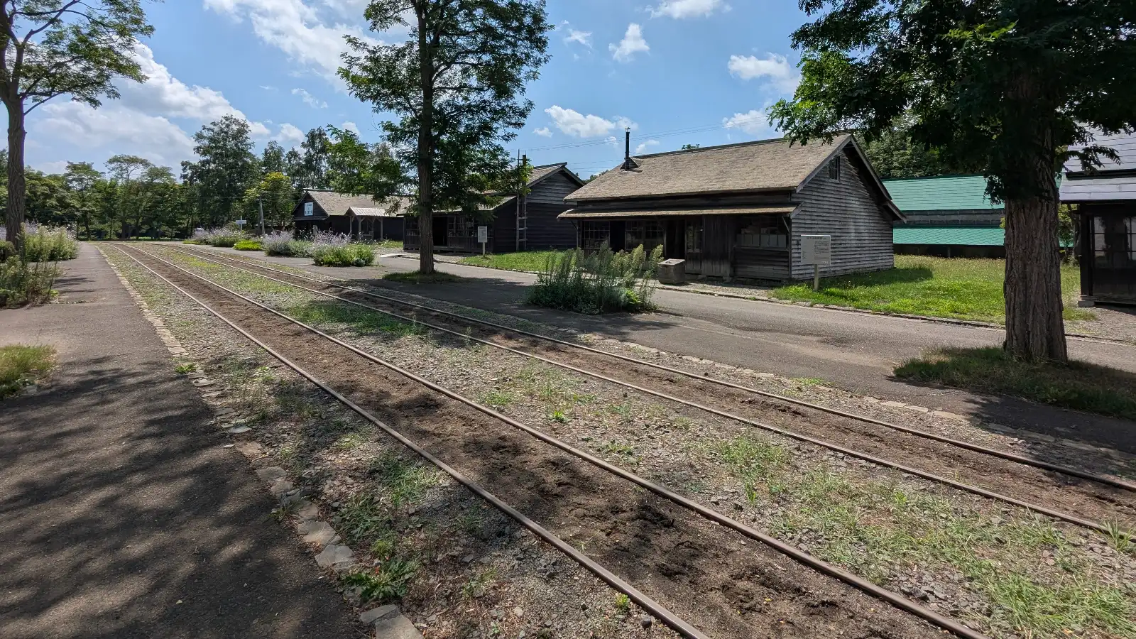 Historic railway street at the Historical Village of Hokkaido with old wooden buildings and train tracks under a bright summer sky.