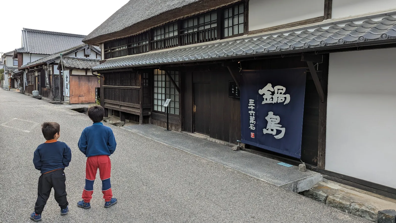 Two boys walk along the preserved Edo-period streets of Hizen Hamashuku in Saga, Japan, exploring old sake breweries and wooden houses.