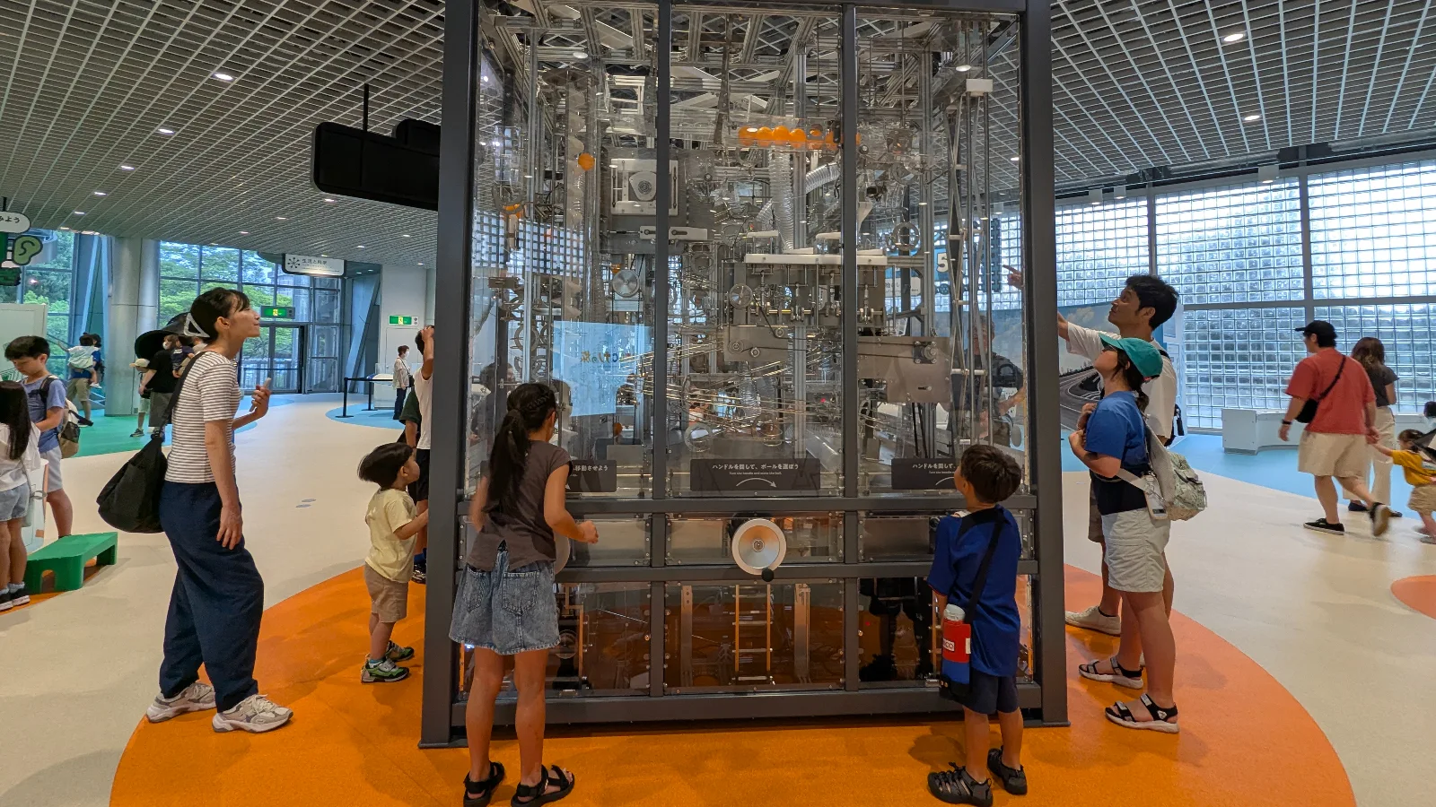Families and children observe the large mechanical ball machine at the Hokushu Sendai City Science Museum, a popular interactive exhibit showing motion and energy in action.