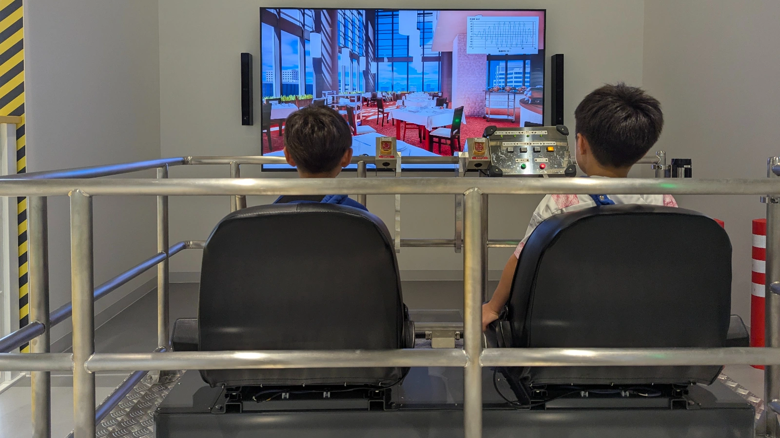 Two children sit in the earthquake simulation ride at the Hokushu Sendai City Science Museum, experiencing how seismic movement feels in real life.