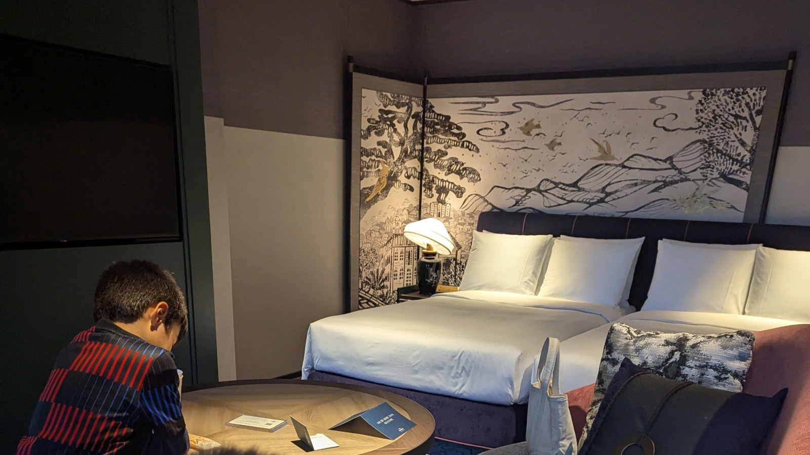 Luca sitting at a table inside a family room at Hotel Indigo Nagasaki, with twin beds and traditional Japanese artwork in the background.