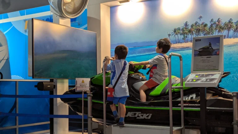 Luca & Nico riding a jet ski simulator at Kobe Maritime Museum, one of the best indoor attractions in Kobe for families with kids.