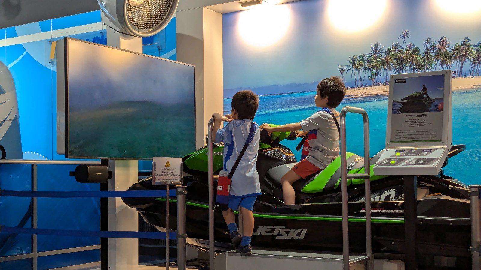 Luca & Nico riding a jet ski simulator at Kobe Maritime Museum, one of the best indoor attractions in Kobe for families with kids.