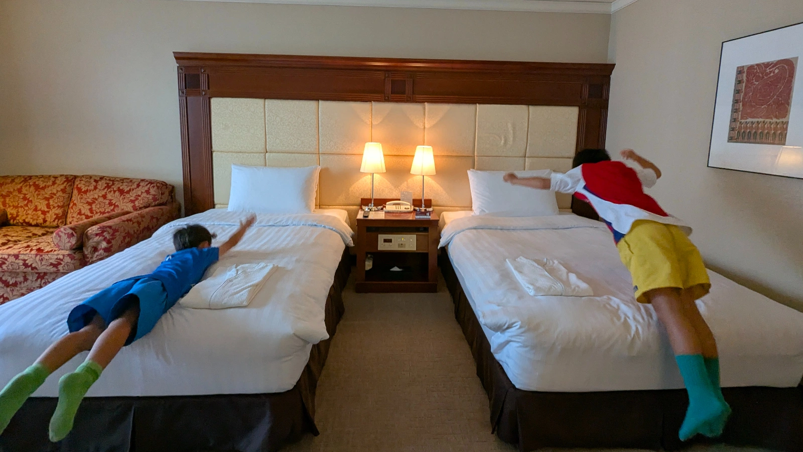 Two children happily jumping onto hotel beds in Japan, capturing the excitement of a family-friendly stay.