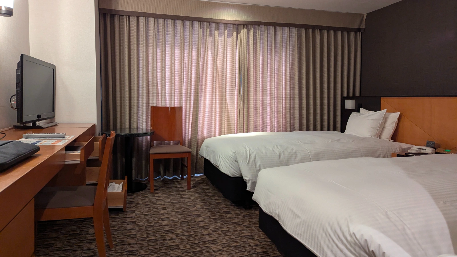 Twin hotel room in Japan with two single beds, work desk, and television, designed for family stays.