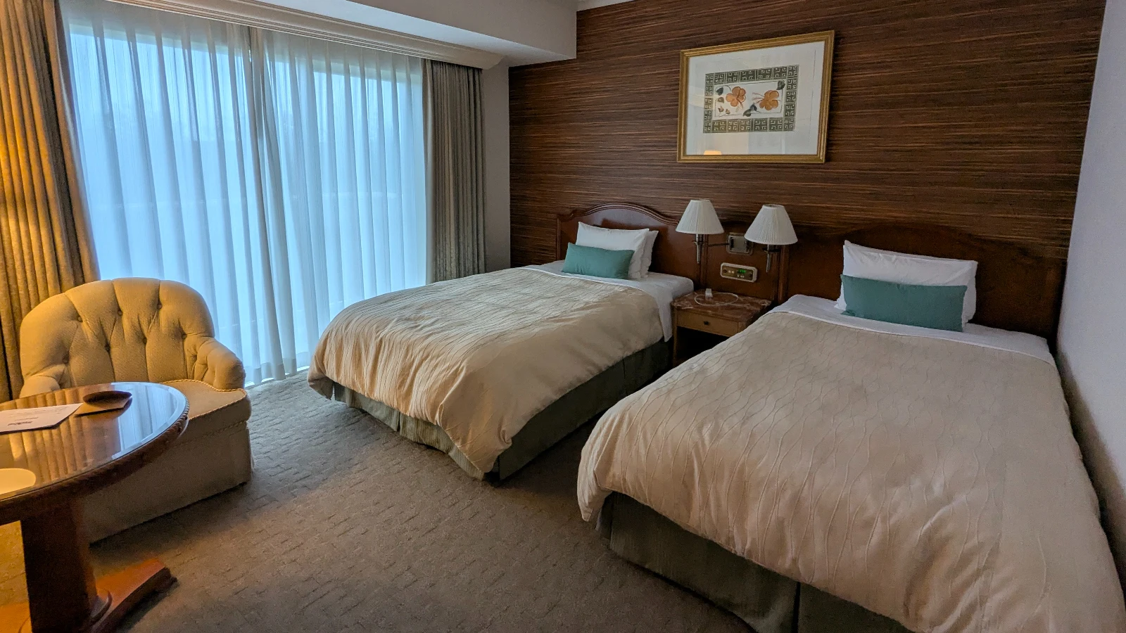 Twin hotel room in Japan with two beds, a sitting chair, and natural light from floor-to-ceiling windows, ideal for families.