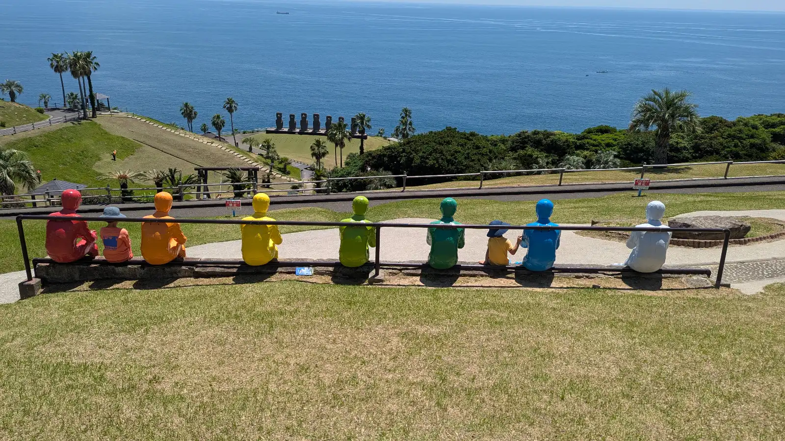Children sitting among colorful statues overlooking the ocean at a Japanese park, a playful and scenic family-friendly garden experience.