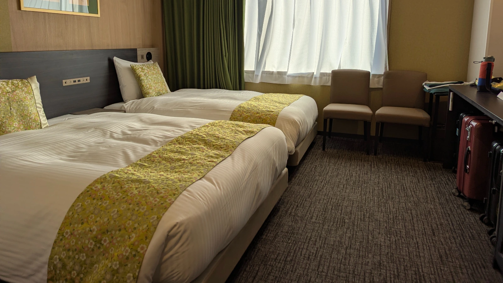 A clean and organized hotel room in Japan featuring two twin beds with green runners and space for luggage, showing a typical family accommodation layout.