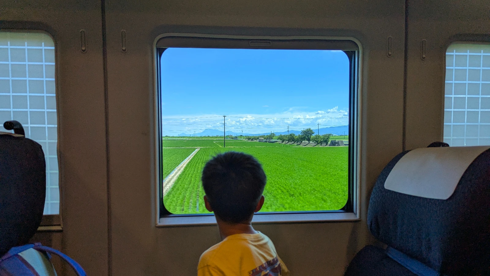 Child looking out a train window at green countryside while traveling through Japan by train with family