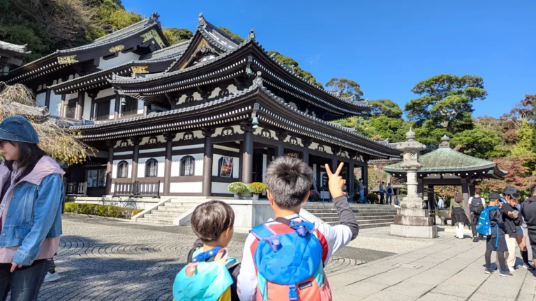 Two kids facing the main hall of Hase Temple in Kamakura, admiring the traditional wooden architecture on a clear day.