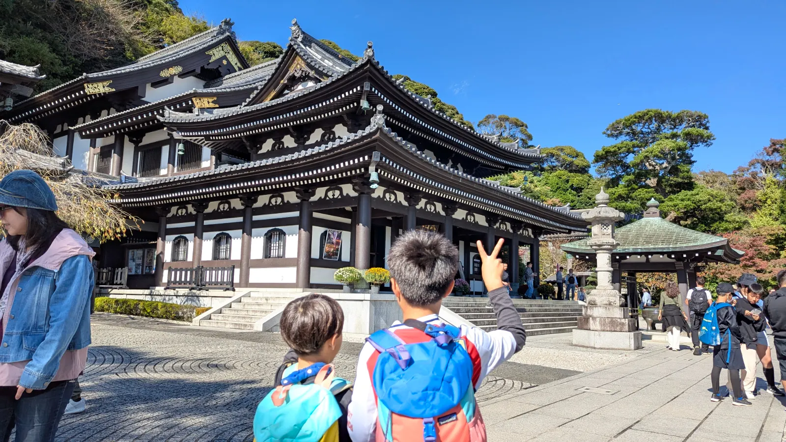 Two kids facing the main hall of Hase Temple in Kamakura, admiring the traditional wooden architecture on a clear day.