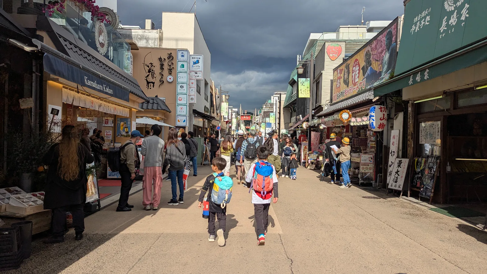 Children walking down Komachi Street in Kamakura, surrounded by shops, snacks, and crowds in the lively shopping district.