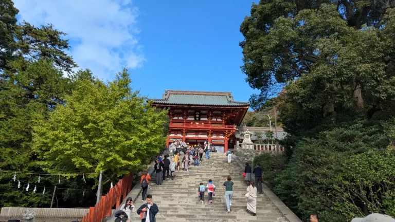 Kids and families climbing the stone steps toward the main hall of Tsurugaoka Hachimangu Shrine in Kamakura on a bright, sunny day.
