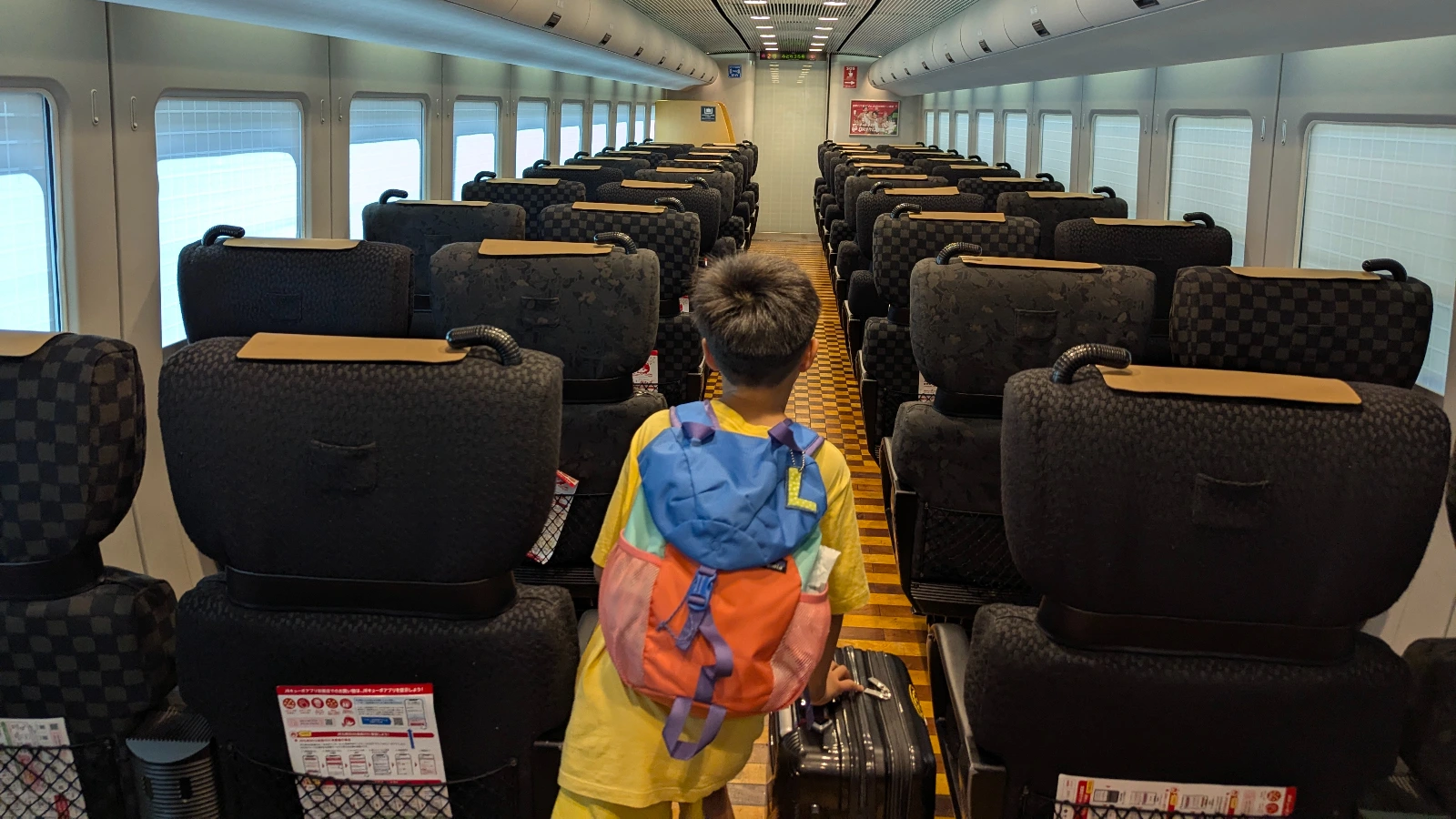 Child pulling a large suitcase down the aisle inside a Shinkansen train in Japan, showing how difficult it can be for families to carry luggage onboard.