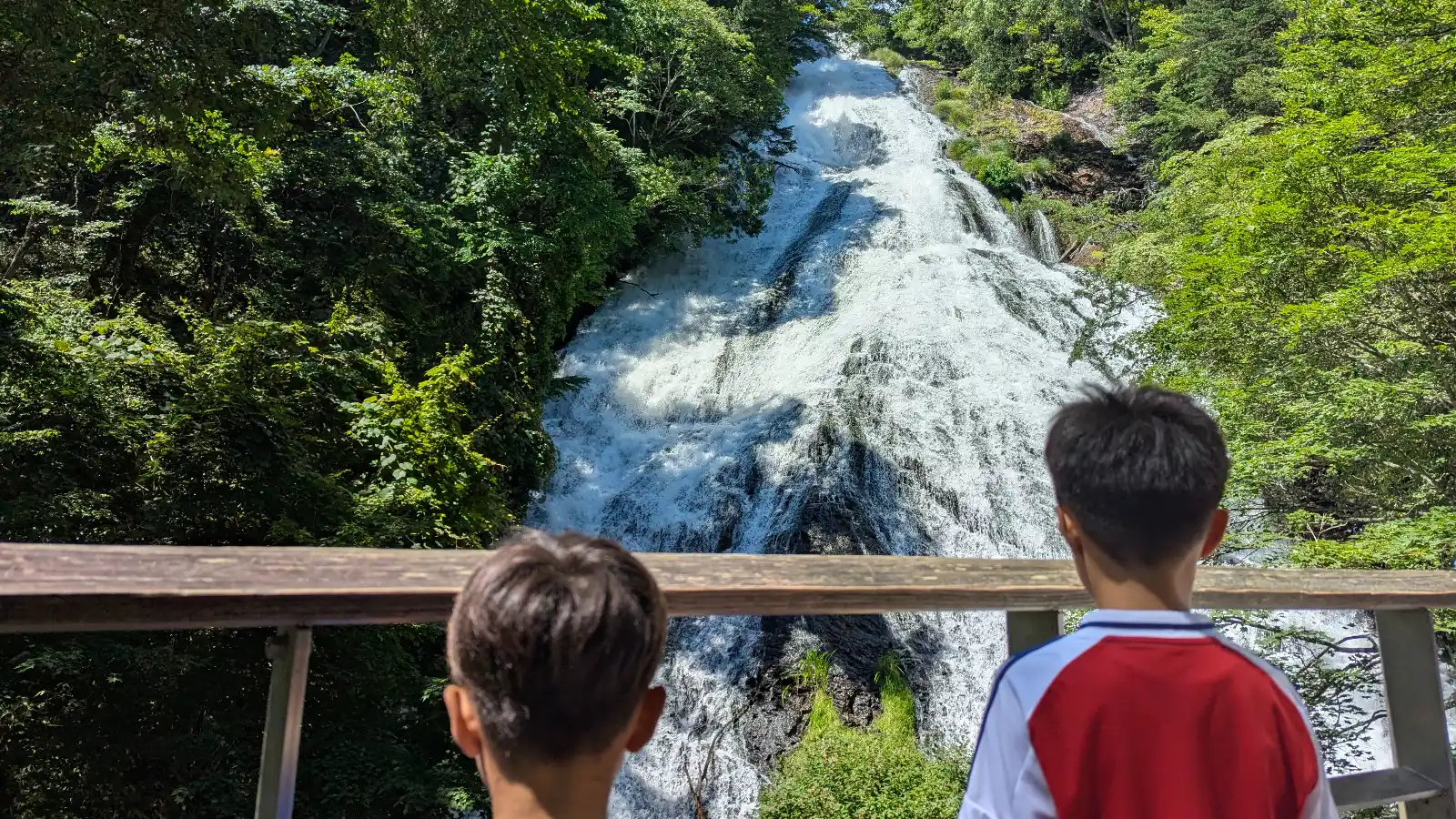 Luca & Nico looking out from the viewing deck at Yudaki Cascades (湯滝) in Nikko, Japan, a family-friendly nature spot.
