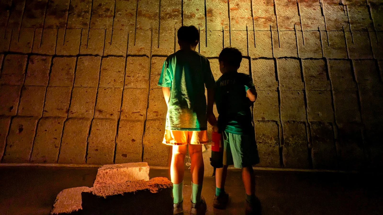 Two children standing near a lit stone wall inside Oya History Museum, learning about Japan’s historic Oya stone quarry in Utsunomiya.