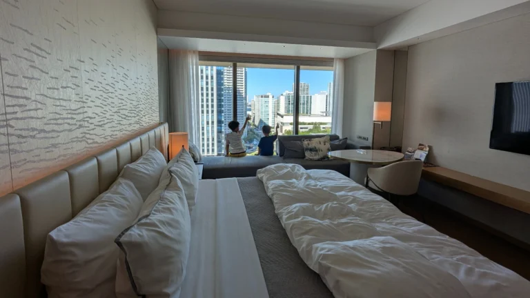 Two children sitting at the window of a Japan hotel room, enjoying a high-rise city view from a family suite.