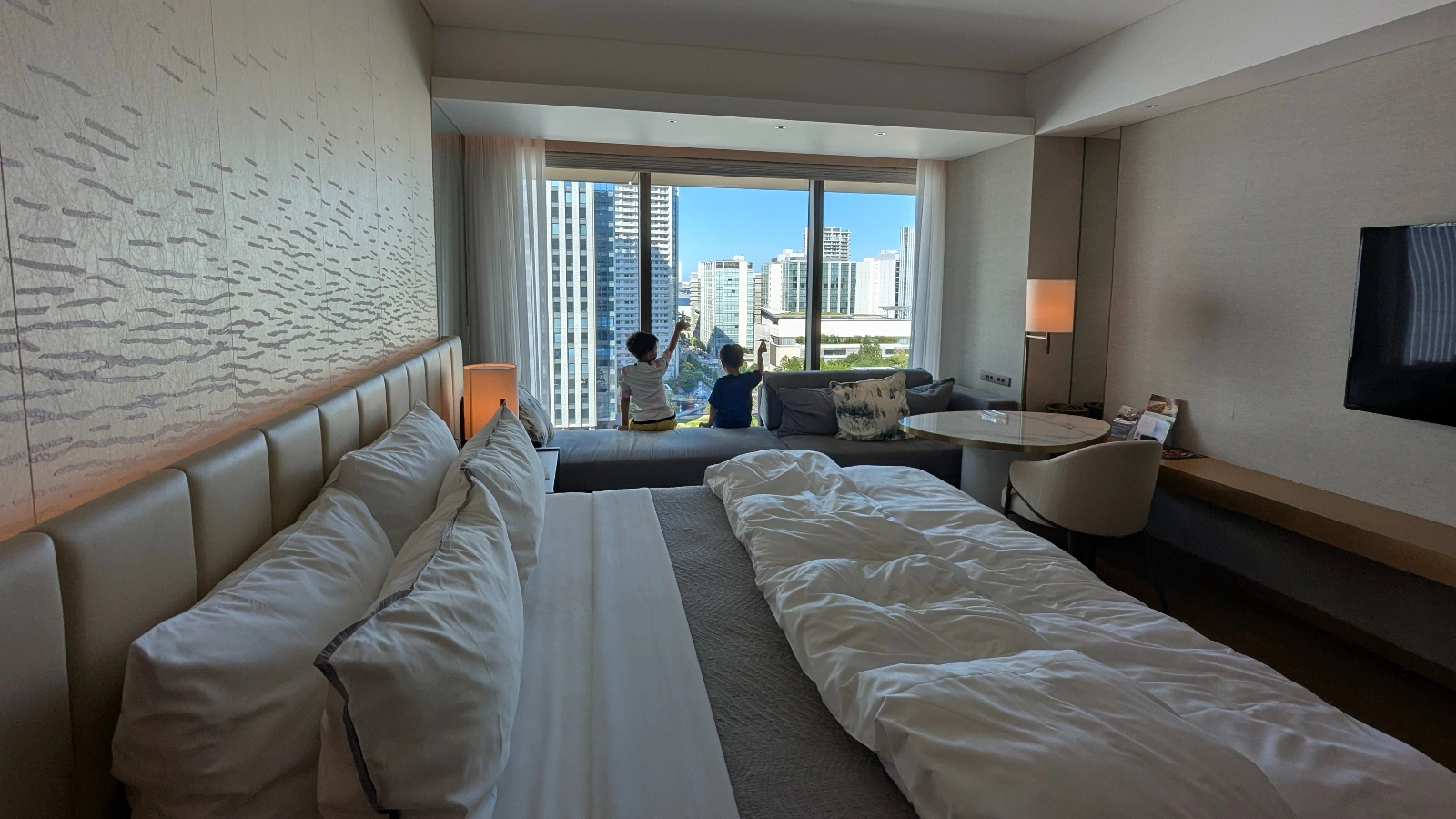 Two children sitting at the window of a Japan hotel room, enjoying a high-rise city view from a family suite.