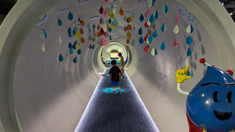 Two children walking through an illuminated pipe tunnel surrounded by hanging paper raindrops at the Sapporo Sewer Museum, Sapporo Japan.