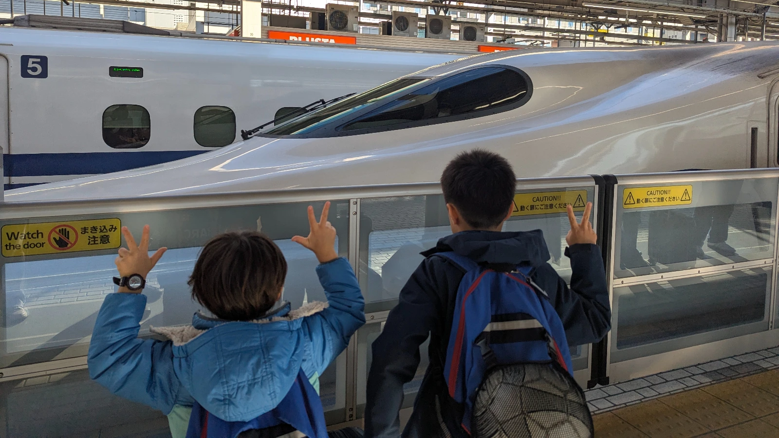 Luca and Nico raising peace signs at a Shinkansen pulling into the platform, train travel in Tokyo with kids