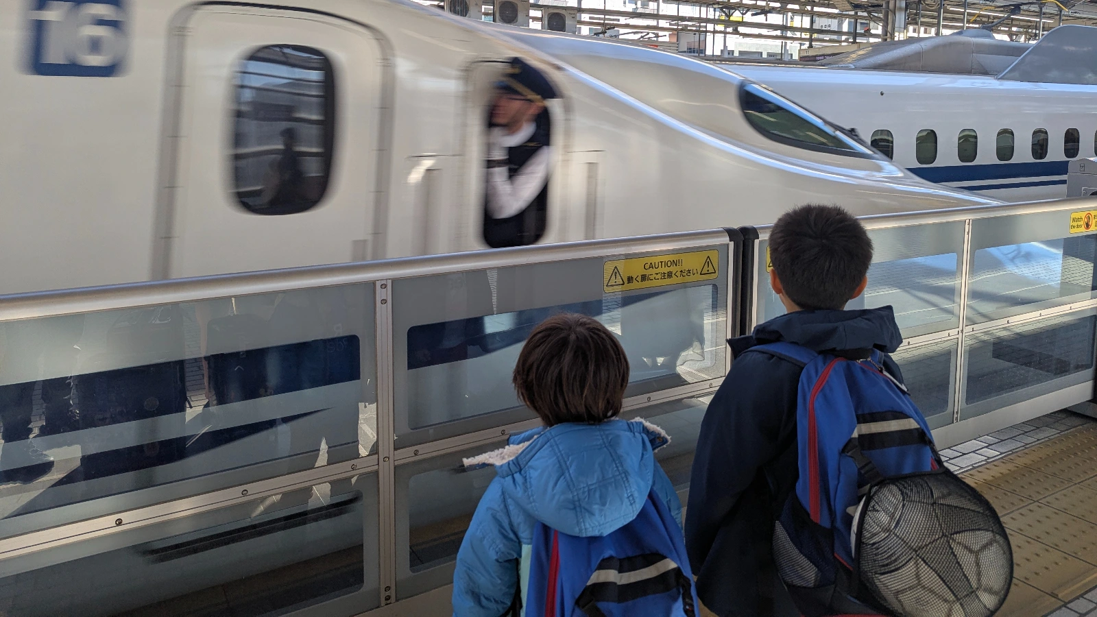 Two children standing on a Japanese train platform watching a Shinkansen bullet train depart, a classic family travel moment experiencing Japan’s high-speed rail with kids.